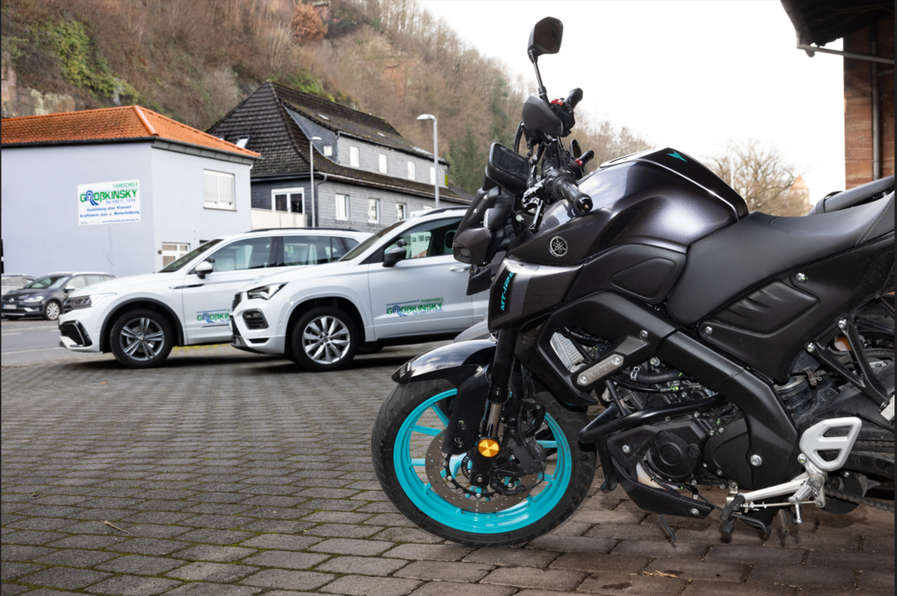 Schwarzes Motorrad mit türkisfarbenen Akzenten neben zwei weißen Autos